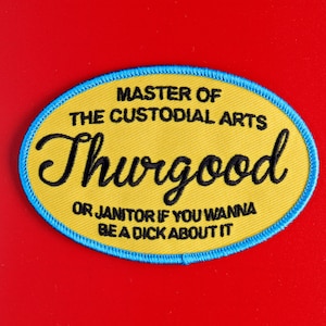 May include: Yellow and blue embroidered patch with the text "MASTER OF THE CUSTODIAL ARTS Thurgood OR JANITOR IF YOU WANNA BE A DICK ABOUT IT" on a red background. The patch is oval-shaped with a blue stitched border.