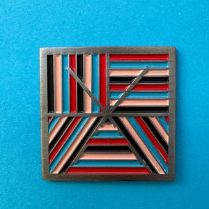 May include: A silver square pin with a geometric design. The design features black, red, pink, and blue stripes that intersect to form a triangle in the center.