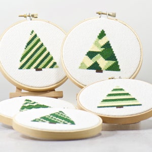 May include: Four embroidery hoops with green and white geometric Christmas tree designs. The hoops are made of wood and have a white fabric background.