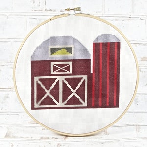 Puede incluir: Un granero rojo y blanco con un silo, bordado en un lienzo blanco en un aro de bordado de madera.