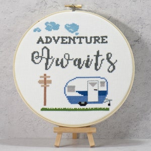 Könnte beinhalten: Stickrahmen-Kunst mit einem blauen und weißen Wohnwagen, einem Holzwegweiser und dem Text "Abenteuer wartet".