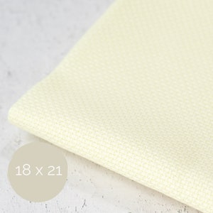 May include: A pale yellow Aida fabric with a distinct grid pattern for cross-stitch projects. The fabric is folded and features a circular overlay with the text 18 x 21, indicating the dimensions in inches for this specific piece of textile material.