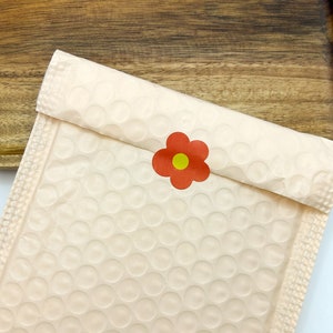 Puede incluir: Un sobre acolchado blanco con una pegatina de flor roja con un centro amarillo.