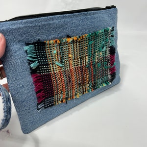 May include: A blue denim zippered pouch with a colorful woven fabric patch sewn on the front.