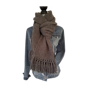 May include: A chunky, hand-knitted scarf in a muted gray color. The scarf features a thick, textured knit and a fringe detail at the ends. The scarf is displayed on a mannequin, draped over a denim jacket.