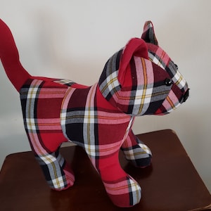 May include: A red, black, and white plaid cat plush toy. The cat is standing on its four legs with its tail curled up behind it.