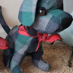May include: A plush toy dog with a green and black plaid pattern and a red and black plaid bandana. The dog has a brown eye and a black nose.
