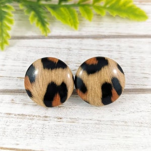 May include: A pair of round, brown, black, and orange leopard print stud earrings.