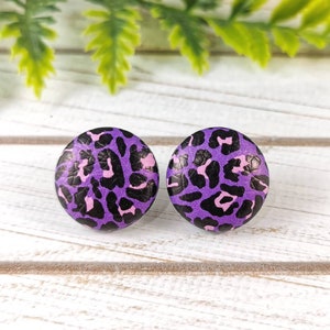 May include: A pair of purple and black leopard print stud earrings. The earrings are round and have a glossy finish.