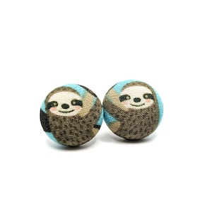 May include: A pair of blue and brown fabric button earrings featuring a smiling sloth design.