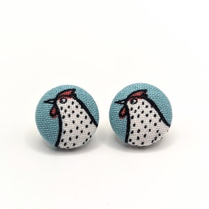 May include: A pair of blue fabric button earrings with a white and black chicken design.
