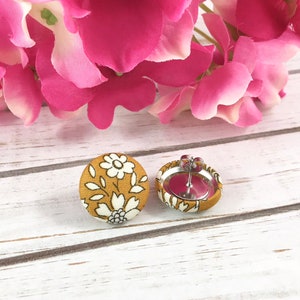 May include: A pair of mustard yellow fabric earrings with a white floral pattern. The earrings have silver posts and backs.