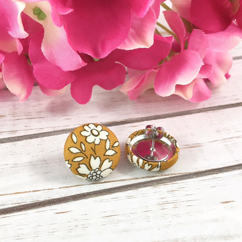 May include: A pair of mustard yellow fabric earrings with a white floral pattern. The earrings have silver posts and backs.