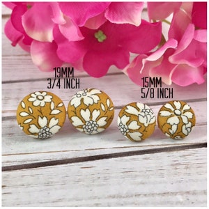 May include: Four fabric covered buttons in two sizes. The larger buttons are 3/4 inch (19 mm) and the smaller buttons are 5/8 inch (15 mm). The buttons have a mustard yellow background with a white floral pattern.