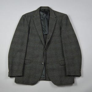 May include: A charcoal grey blazer featuring a dark plaid pattern, notched lapels, two front buttons, and two flap pockets. The garment is fully lined with a smooth black interior fabric and includes long sleeves with buttoned cuffs.
