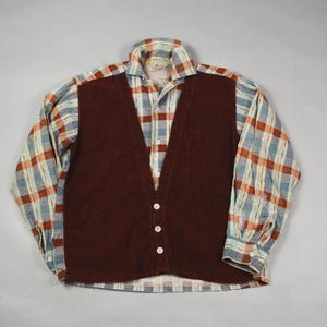 May include: A vintage button-down shirt with a corduroy vest overlay. The shirt features a plaid pattern in shades of blue, orange, and white. The vest is a solid, deep burgundy color. The shirt has long sleeves and a collared neckline.