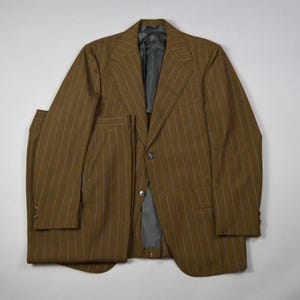 May include: A brown suit featuring a subtle vertical pinstripe pattern in a lighter shade. The set includes a single-breasted blazer with notched lapels, two front buttons, and long sleeves, paired with matching trousers that have a straight-leg cut.