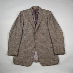 Peut inclure: Un blazer en tweed marron avec une fermeture à deux boutons, deux poches avant et des poignets boutonnés. Le blazer a un revers cranté et une doublure en satin. Le tissu a un aspect texturé.