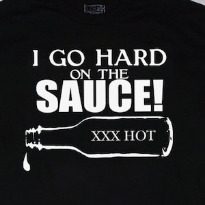 May include: Black t-shirt with white text that reads "I go hard on the sauce!" and a white silhouette of a hot sauce bottle with the text "XXX HOT" on it.