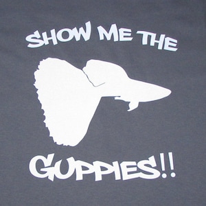May include: A gray t-shirt with white text that reads "Show me the guppies!" and a white silhouette of a fish.