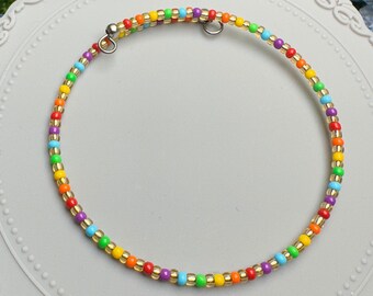 May include: A rainbow beaded bracelet with gold accents. The bracelet is on a gray, decorative plate.