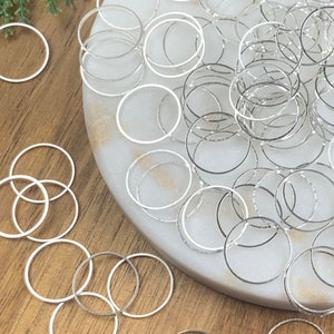 Puede incluir: Un mont&oacute;n grande de anillos de salto plateados sobre una superficie de m&aacute;rmol blanco. Los anillos de salto est&aacute;n dispersos alrededor de la superficie, algunos se superponen. Los anillos de salto son todos del mismo tama&ntilde;o y forma.