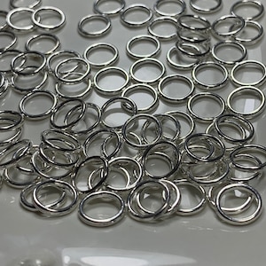 May include: A pile of silver jump rings, a type of jewelry finding, on a white plate.
