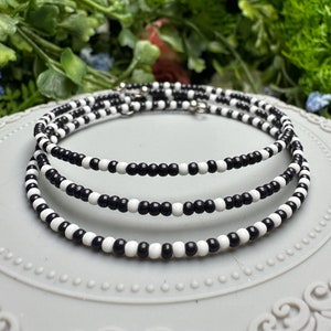 May include: Three black and white beaded necklaces layered on a white plate. The beads are small and round, creating a striped pattern.