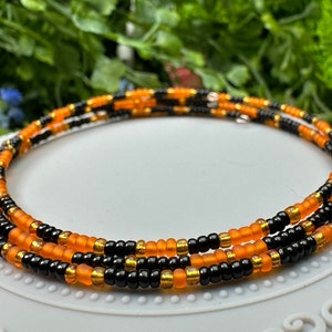 May include: A black and orange beaded necklace with gold accents. The necklace is made of small, round beads and is layered in a repeating pattern.
