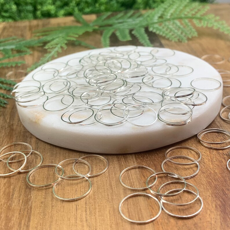 Puede incluir: Un mont&oacute;n grande de anillos de salto plateados sobre una superficie de m&aacute;rmol blanco. Los anillos de salto est&aacute;n dispersos sobre una superficie de madera.