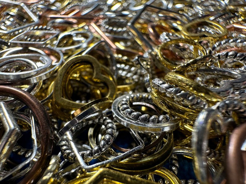May include: A close-up of a pile of various metal charms and pendants in gold, silver, and copper tones. The charms are in different shapes, including circles, hearts, and squares. Some of the charms have intricate designs, while others are plain.
