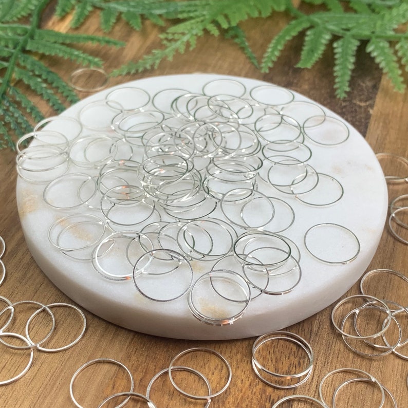 Puede incluir: Un mont&oacute;n de anillos de salto plateados sobre una superficie de m&aacute;rmol blanco. Los anillos de salto est&aacute;n dispuestos en un patr&oacute;n aleatorio y todos son del mismo tama&ntilde;o.