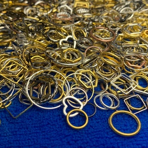 May include: A large assortment of metal rings and shapes in gold, silver, and copper tones. The rings and shapes are scattered on a blue surface.