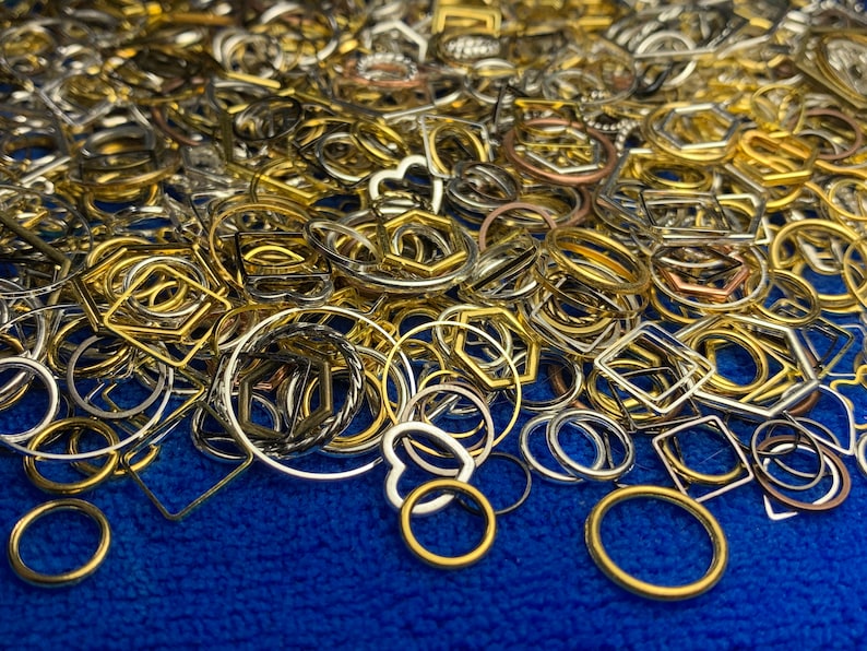 May include: A large assortment of metal rings and shapes in gold, silver, and copper tones. The rings and shapes are scattered on a blue surface.