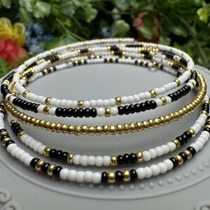 May include: A multi-strand beaded necklace with black, white, and gold beads. The necklace is layered and has a simple design.