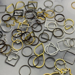 May include: Assortment of metal jump rings in various shapes and sizes, including circles, squares, teardrops, and stars. The jump rings are in gold, silver, and bronze tones.