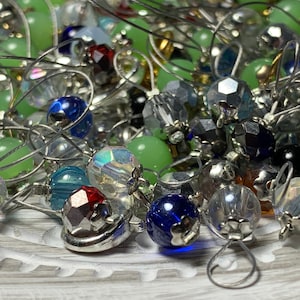 May include: A collection of colorful glass beads with silver wire loops. The beads are in various shapes and sizes, including round, faceted, and teardrop.