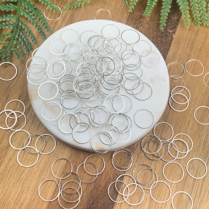 Puede incluir: Un mont&oacute;n grande de anillos de salto plateados sobre una superficie de m&aacute;rmol blanco. Los anillos de salto est&aacute;n dispersos alrededor de la superficie, algunos se superponen. Los anillos de salto son todos del mismo tama&ntilde;o y forma.