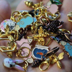 May include: A collection of gold-tone charms featuring various designs, including a bee, a fishbowl with a fish, a pig, a bunny, and a sheep. The charms are attached to a gold chain and are perfect for adding a touch of whimsy to a bracelet or necklace.