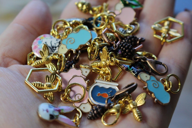 May include: A collection of gold-tone charms featuring various designs, including a bee, a fishbowl with a fish, a pig, a bunny, and a sheep. The charms are attached to a gold chain and are perfect for adding a touch of whimsy to a bracelet or necklace.