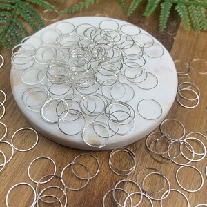 Puede incluir: Un mont&oacute;n grande de anillos de salto plateados sobre una superficie blanca. Los anillos de salto est&aacute;n dispuestos en un patr&oacute;n aleatorio y todos son del mismo tama&ntilde;o. Tambi&eacute;n hay algunos anillos de salto dispersos alrededor del mont&oacute;n.