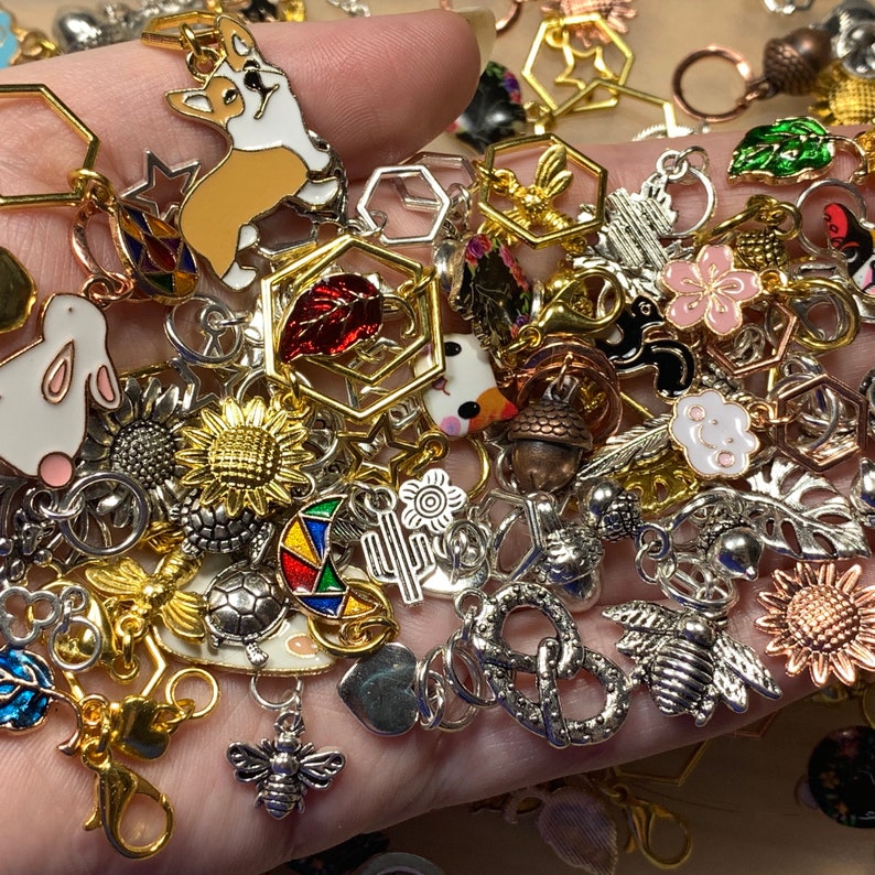 A completely random assortment of colorful  metal, enamel, and acrylic stitch markers held in a hand