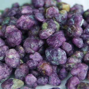 May include: A pile of purple and green rough ruby gemstones. The stones are various sizes and shapes.