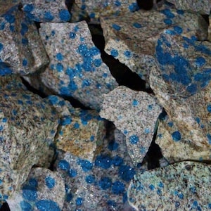 Könnte beinhalten: Nahaufnahme eines Haufens rauer, grauer und weißer Steine mit blauen Flecken. Die Steine haben ein gesprenkeltes Aussehen.