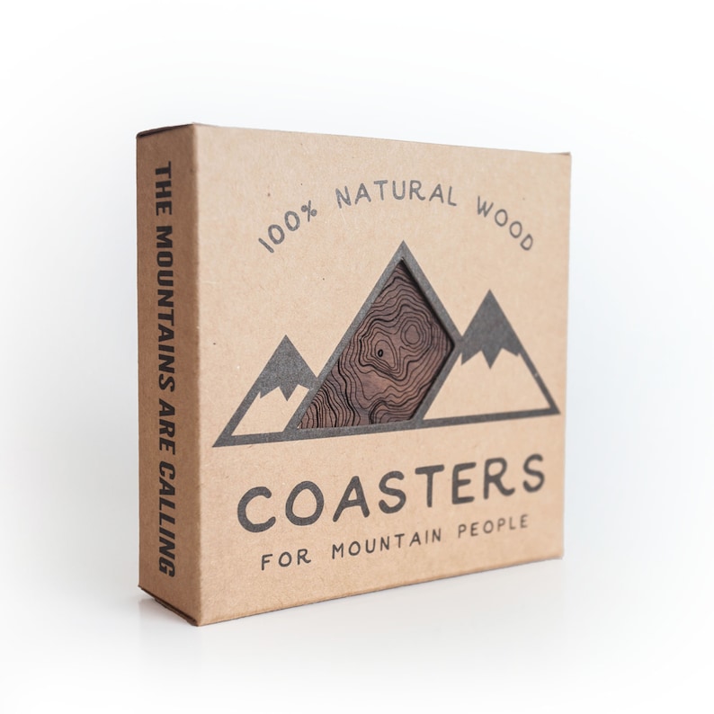 May include: A brown cardboard box with the text "THE MOUNTAINS ARE CALLING" on the side. The front of the box has a graphic of mountains with the text "100% NATURAL WOOD" and "COASTERS FOR MOUNTAIN PEOPLE".