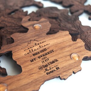 May include: Wooden map of Mount Everest, part of the "Mountain Collection - World Series" series. The map is made by Kegs & Cute Co. in Olympia, WA. The map is made of wood and has a brown finish.