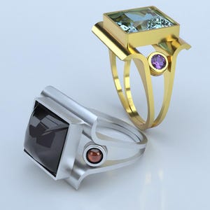 May include: Two rings with square gemstones. One ring is gold with a light blue gemstone and a purple accent stone. The other ring is silver with a dark gemstone and a red accent stone. Both rings have a modern design.