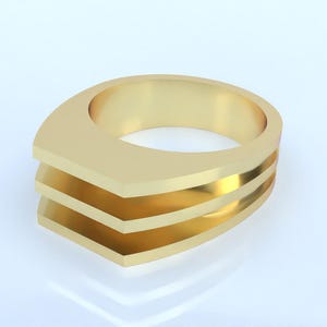 Puede incluir: Un anillo dorado con un diseño único. El anillo presenta una parte superior plana y rectangular con tres bandas horizontales en capas. El anillo está hecho de un material metálico brillante y está sobre un fondo blanco.