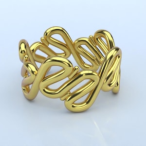 May include: A gold-colored ring with a repeating, openwork design. The ring features a series of interconnected, stylized loops, creating a continuous pattern around the band. The ring is displayed on a white surface.