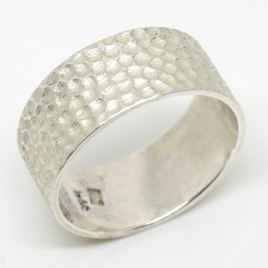 May include: A silver ring with a textured hammered finish. The ring is wide and has a smooth inner band.